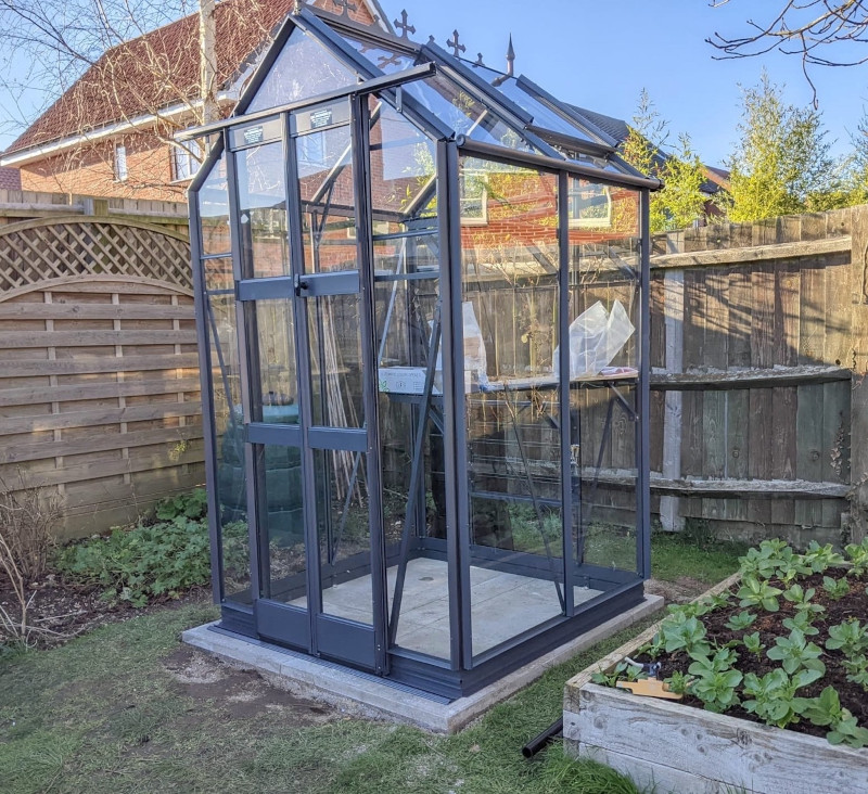<strong>MAXIM:</strong> A 4’3 (1300mm) wide model in lengths from 4’5 (1351mm) onwards. It is compact in size but has tall eaves of 5’8 (1726mm) and double doors which provide an opening of 6’3 x 2’ (1910mm x 600mm) ensuring a good working space. Pictured is a 4ft 3in x 4ft 5in MAXIM in Anthracite colour, with staging, shelf, cresting & finials. 5ft 8in high side walls give good growing room in this model.