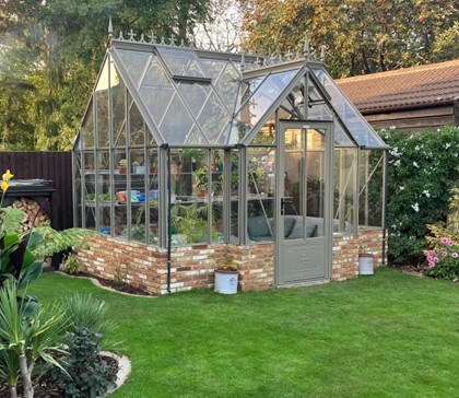 <strong>Rushby VICTORIAN:</strong> An 9ft 7in (2935mm) deep Victorian model with porch in a coloured finish. Large pane 4mm toughened safety glass and bar capping included. Extremely strong box section framework. Locking hinged door. Various lengths available from 8’ 8 (2632mm) onwards. 10’1 (3078mm) ridge height. Staging, shelving, cresting options. With dwarf wall.