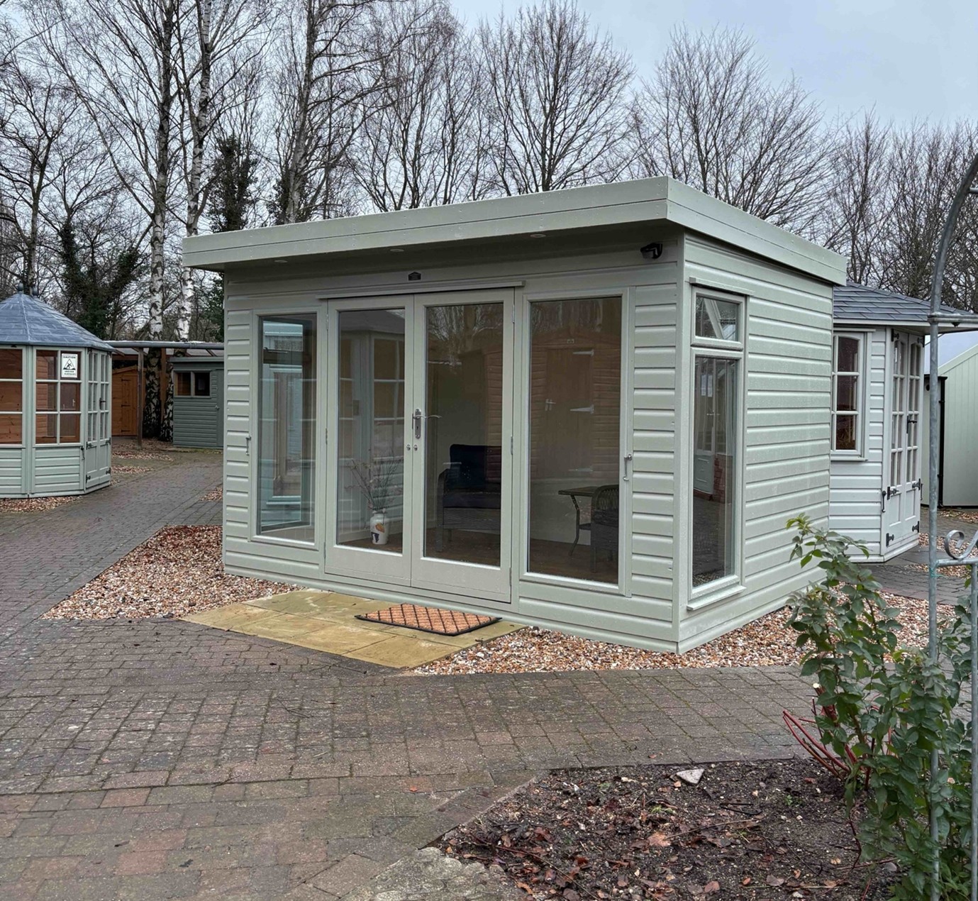 Ely Garden Room 12ft x 8ft (3.6m x 2.4m).  Insulated and with optional painted internal lining, side windows with top opening vents, vinyl tile flooring, guttering, electrics and exterior paint finish.